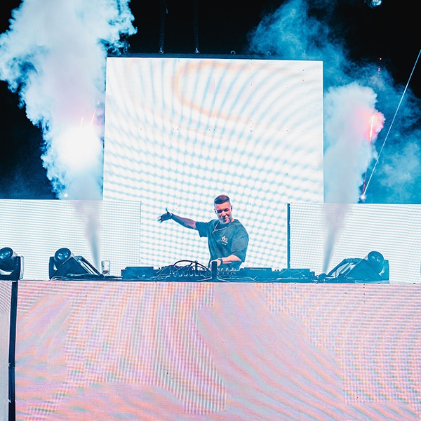 Tiscore performing live on a large stage with bright LED screens and festival production lighting.