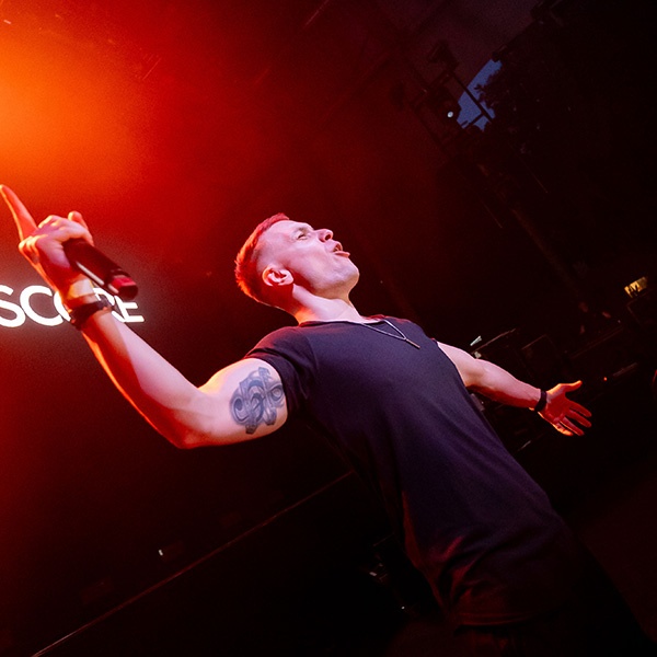 Tiscore hyping the crowd during a live DJ set with dramatic stage lighting and energy.